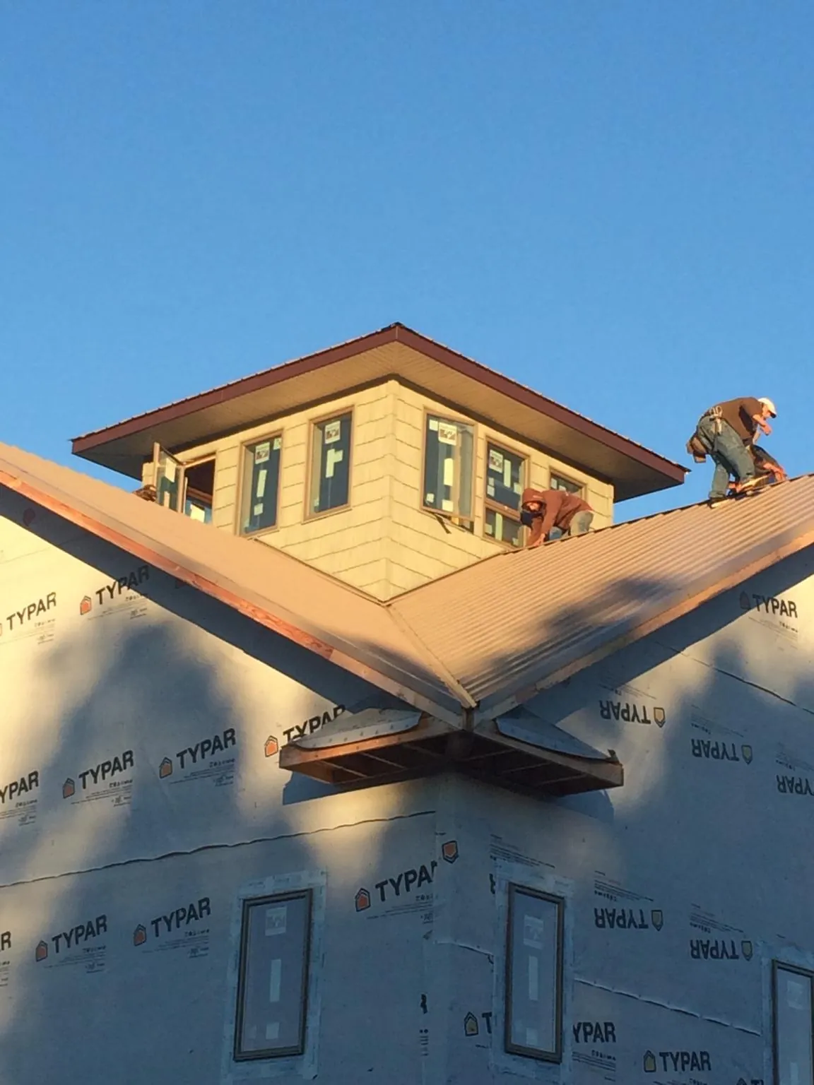 Roofers working around a rooftop cupola on a new metal roof at sunset in Sparks